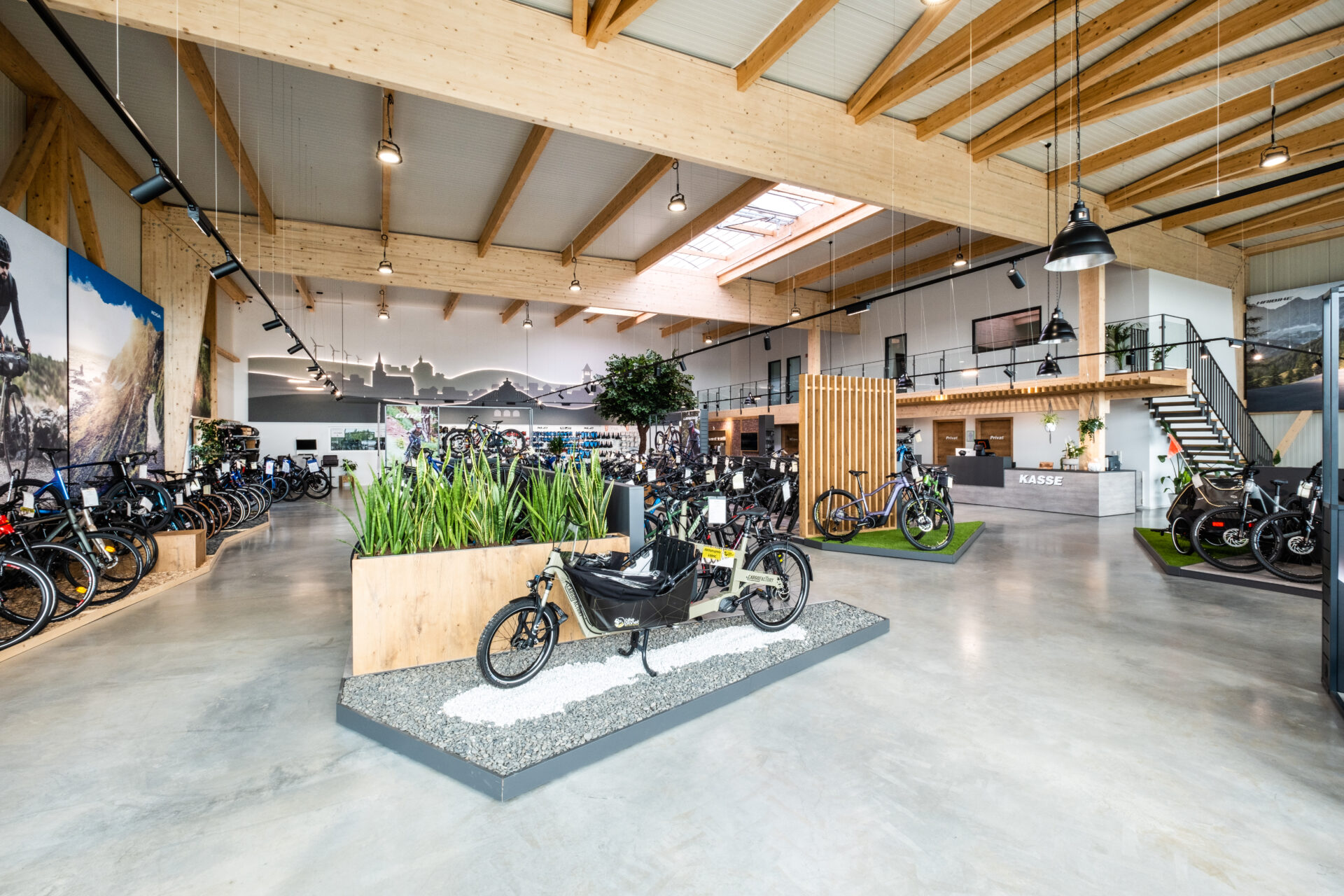 Fahrrad-Ausstellung immersiv: Zonierung mit Bodenelementen (Kies-Optik) und Stadt-Silhouetten, mit nahtlosem Übergang zur Kasse.